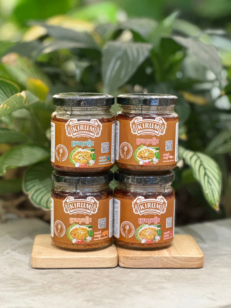 Four jars of Kirum prahok ktiss displayed on wooden boards with a greenery background
