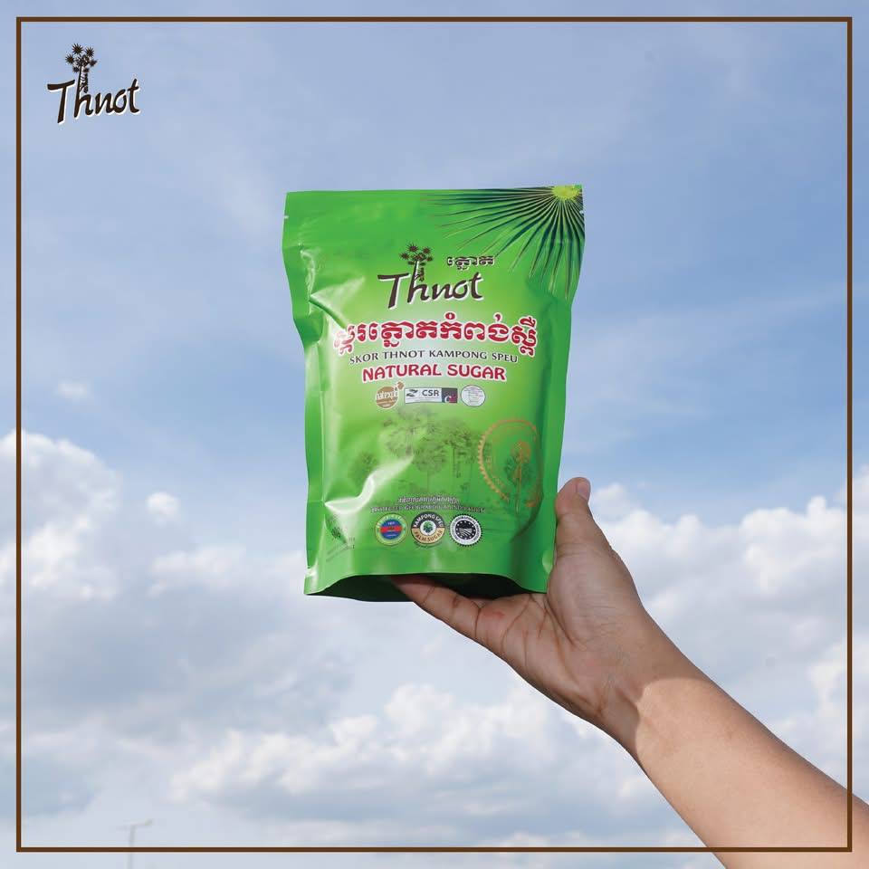 Hand holding a green bag of Thnot Kampong Speu natural sugar against a blue sky